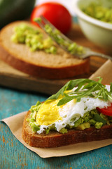 Tasty sandwich with egg, avocado and vegetables on paper napkin, on color wooden background