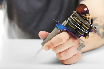 Hand of tattoo artist with tattoo machine at white table, closeup