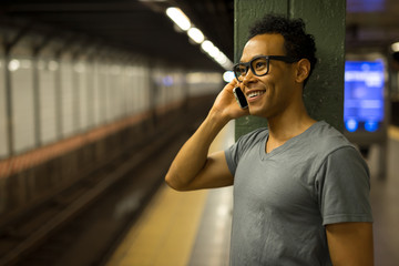 Young African Asian man in New York City at night talking cell phone in subway