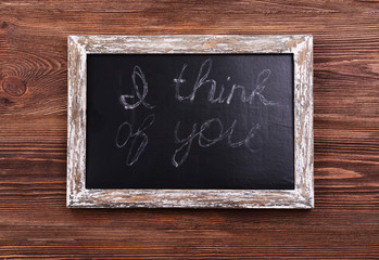 Inscription I THINK OF YOU on blackboard on wooden background