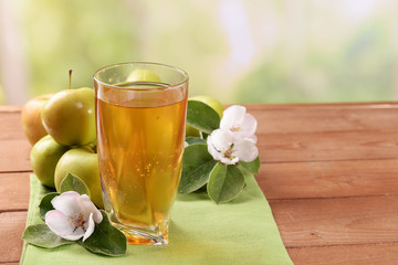 Glass of apple juice and apples on wooden table, on nature background