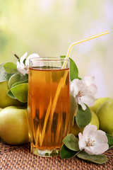 Glass of apple juice and apples on wooden table, on nature background