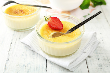 Creme brulee dessert with fresh strawberries and mint leaves, on color wooden background