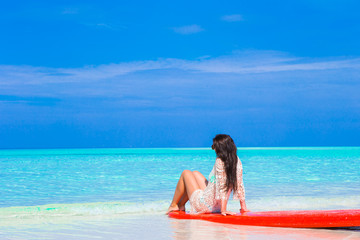 Young surfer woman at white beach on red surfboard