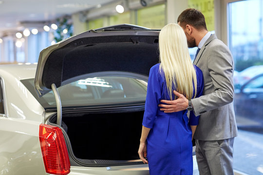 happy couple choosing car in auto show or salon
