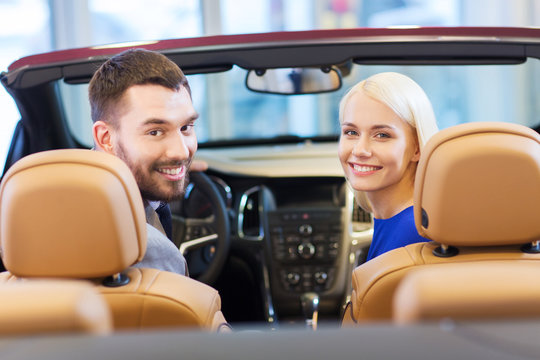 happy couple sitting in car at auto show or salon