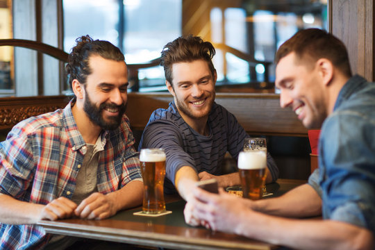 male friends with smartphone drinking beer at bar