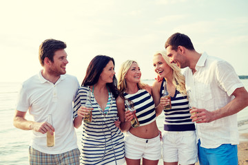 smiling friends with drinks in bottles on beach