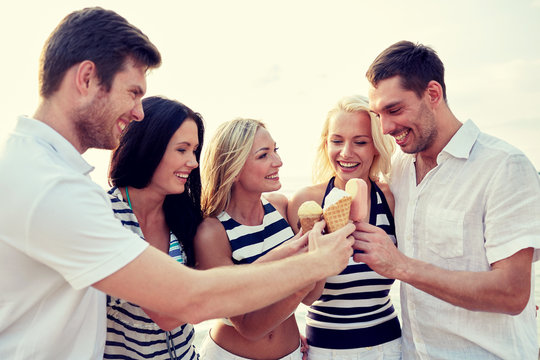 smiling friends eating ice cream on beach