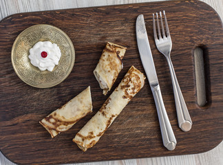 Traditional sweet pancakes on wooden plate.
Two fried pancakes with cheese one cut down cream white with red berry folk and knife rough country wood background