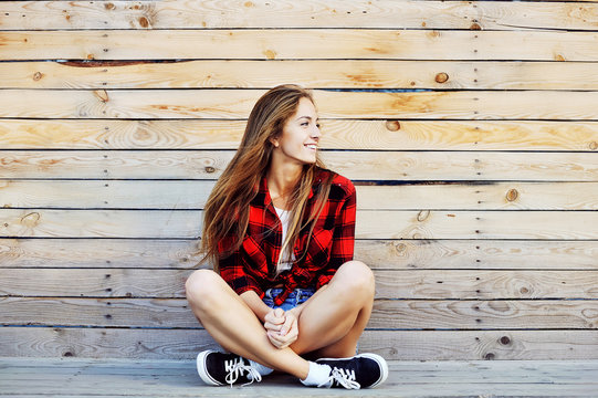 Smiling hipster girl sitting on the wooden porch and looking at