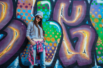 beautiful cool girl in hat and sunglasses over graffiti wall