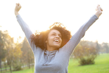 Cheerful young woman smiling with arms raised - Powered by Adobe