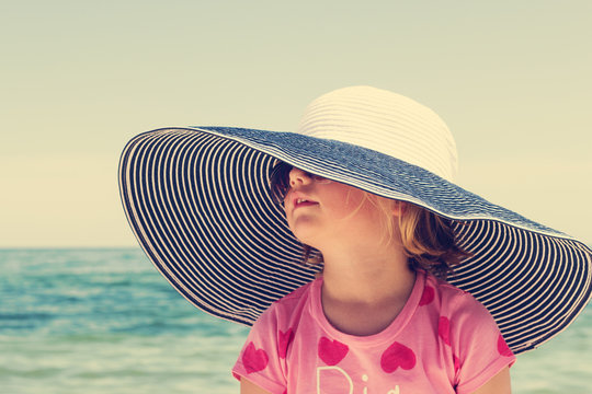 Funny little girl in a big striped hat on the beach. The image i