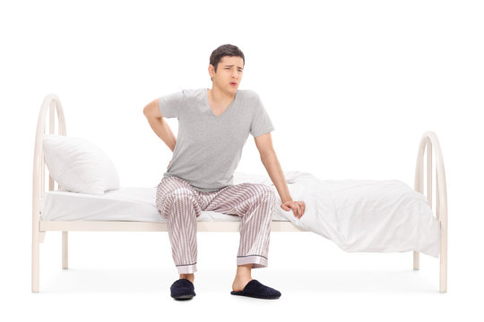 Young man having a back pain seated on a bed