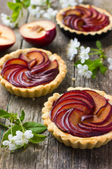 Tartlets with plum on wooden background