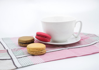 Colorful macarons with white cup and plate on pink cloth.