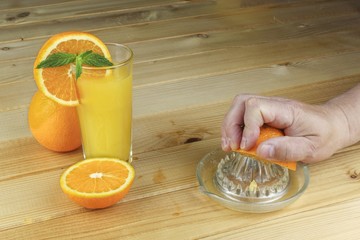 A hand squeezing juice from an orange on a manual glass squeezer. Set on a wooden planked table.