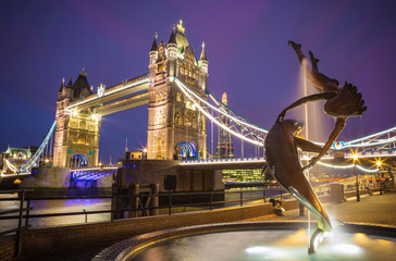London, United Kingdom - The lady and the dolphin fountain with the iconic illuminated Tower Bridge at night