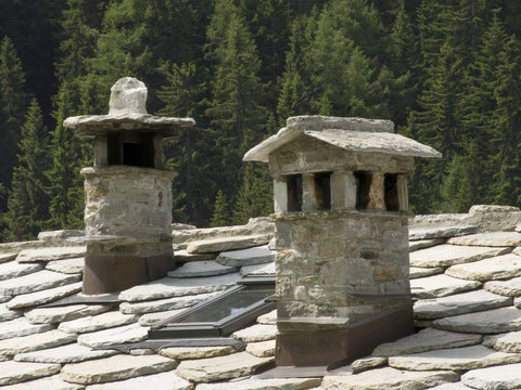 Foto Stock i camini di pietra sul tetto della baita alpina | Adobe Stock