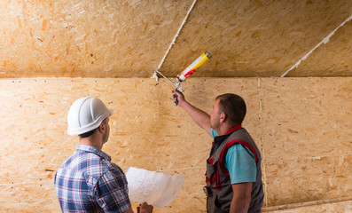 Foreman Watching Worker Apply Caulking in New Home