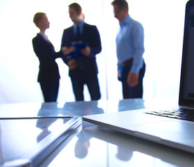 Laptop  computer on  desk , three businesspeople standing in the