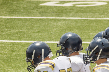 Fototapeta premium Kids standing on a football field with black helmets and white jerseys 