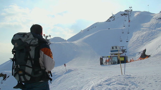 Tourist with backpack looking at snowy skiing run on mountains