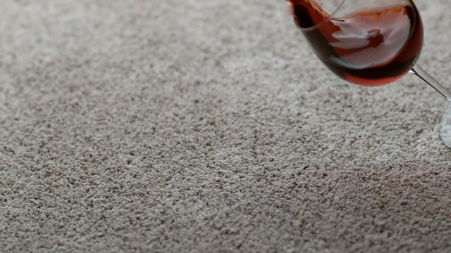 Glass of red wine spilling on carpet in slow motion
