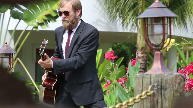 bearded man in black suit plays guitar actively and goes out	