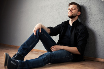 Young man in shirt siting with hands clasped against a wall