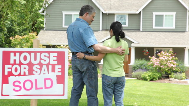 Couple look at new home, SOLD sign in foreground
