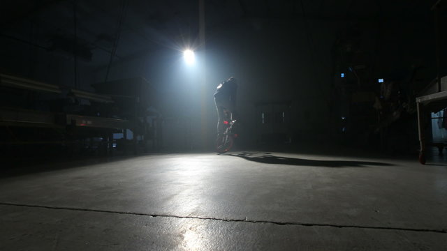 BMX rider doing tricks in dark warehouse.