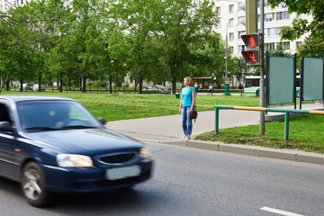 Young woman stands at traffic light and waiting for green signal