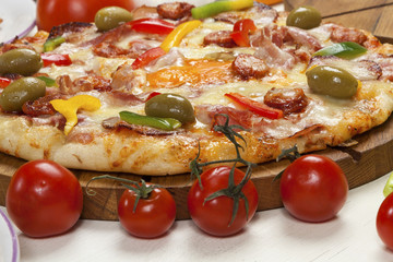 Pizza with several kinds of meat products, mushrooms and cheese served beside cherry tomatoes.