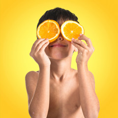 Child holding two slice oranges like glasses