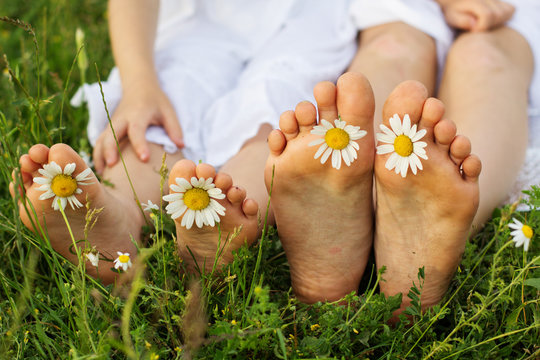 Childs feets with daisy flowers on green grass 
