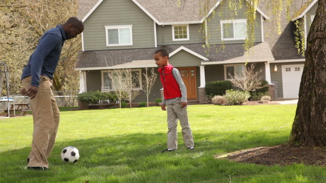 Father and son kick ball in front of family home