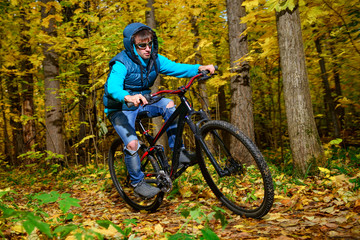 Cyclist extreme riding mountain bike through impassable dried bushes in wild autumn colorful forest 