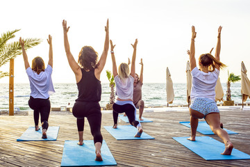 group of young females practicing yoga on the seaside during the sunrisе