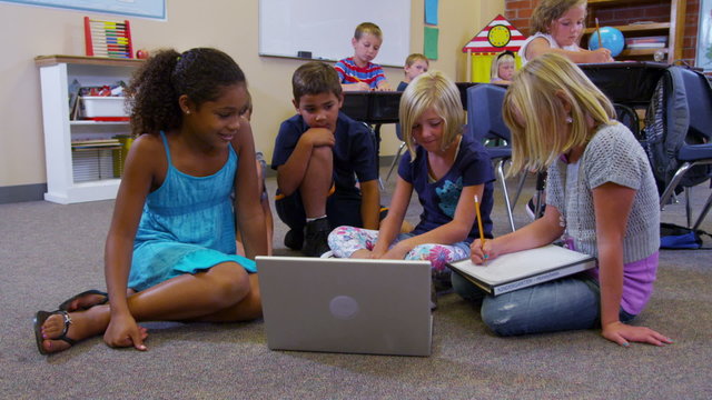 Elementary school students look at laptop computer together