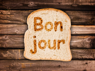 Word bonjour (meaning good morning in French) written on a toasted slice of bread © Delphotostock