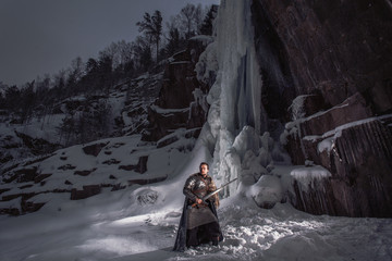 Medieval knight with sword standing in rocky winter landscape