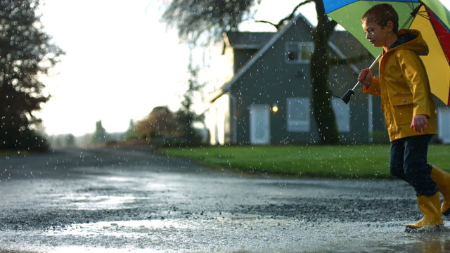 Young boy running through puddles with umbrella, slow motion