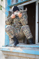 Military camouflage with a rifle on a background of bombed buildings.