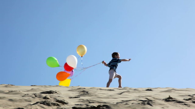 Boy running on sand dune with balloons