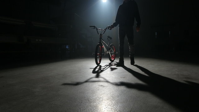BMX rider doing tricks in dark warehouse.