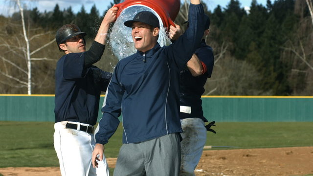 Baseball players pour cooler of water over coach, slow motion