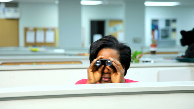 Businesswoman peeks over cubicle with binoculars