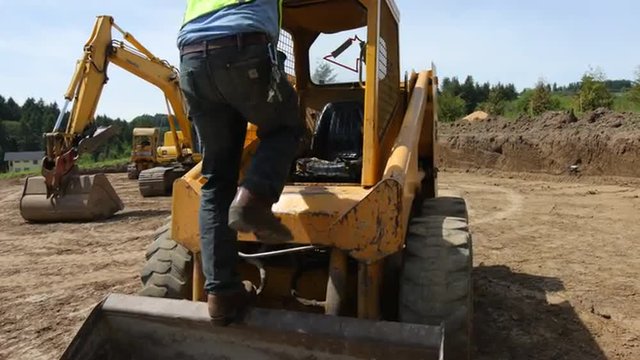Worker climbs into skid steer excavator